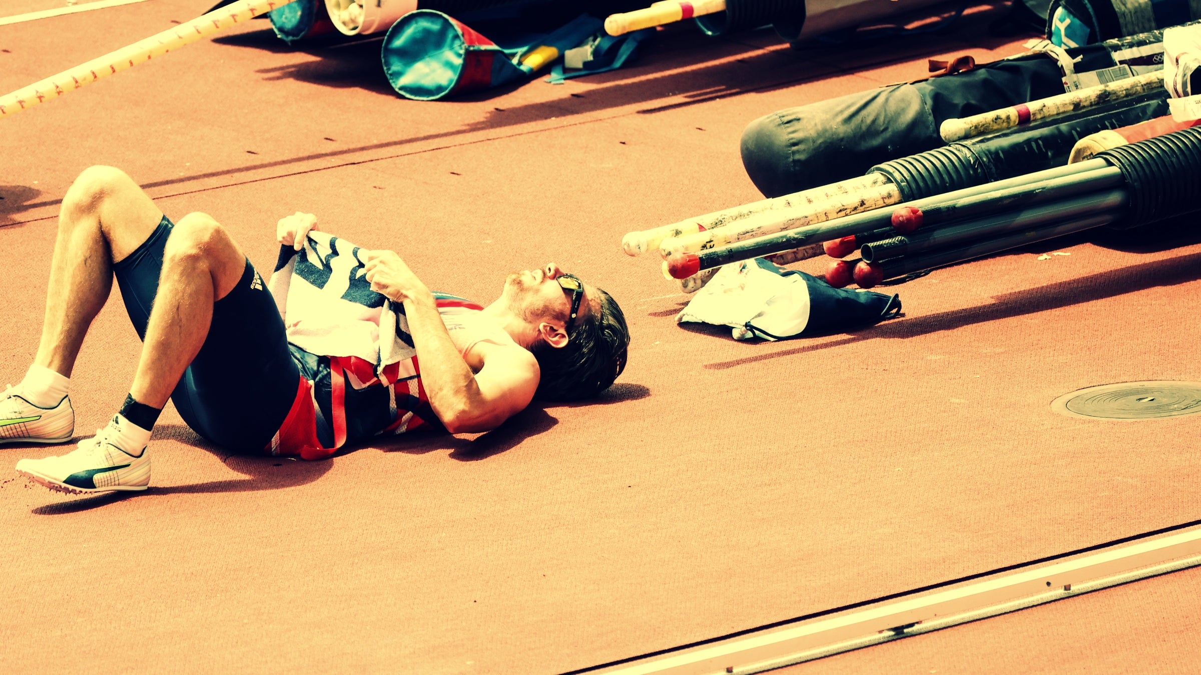 Male runner lies down on his back on track while lifting shirt in the heat
