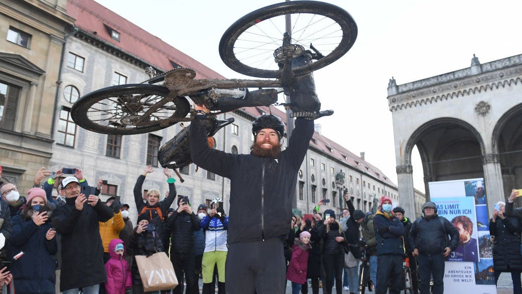 German extreme athlete Jonas Deichmann lifts his bike into the air at Odeonsplatz at the finish of his triathlon around the world.