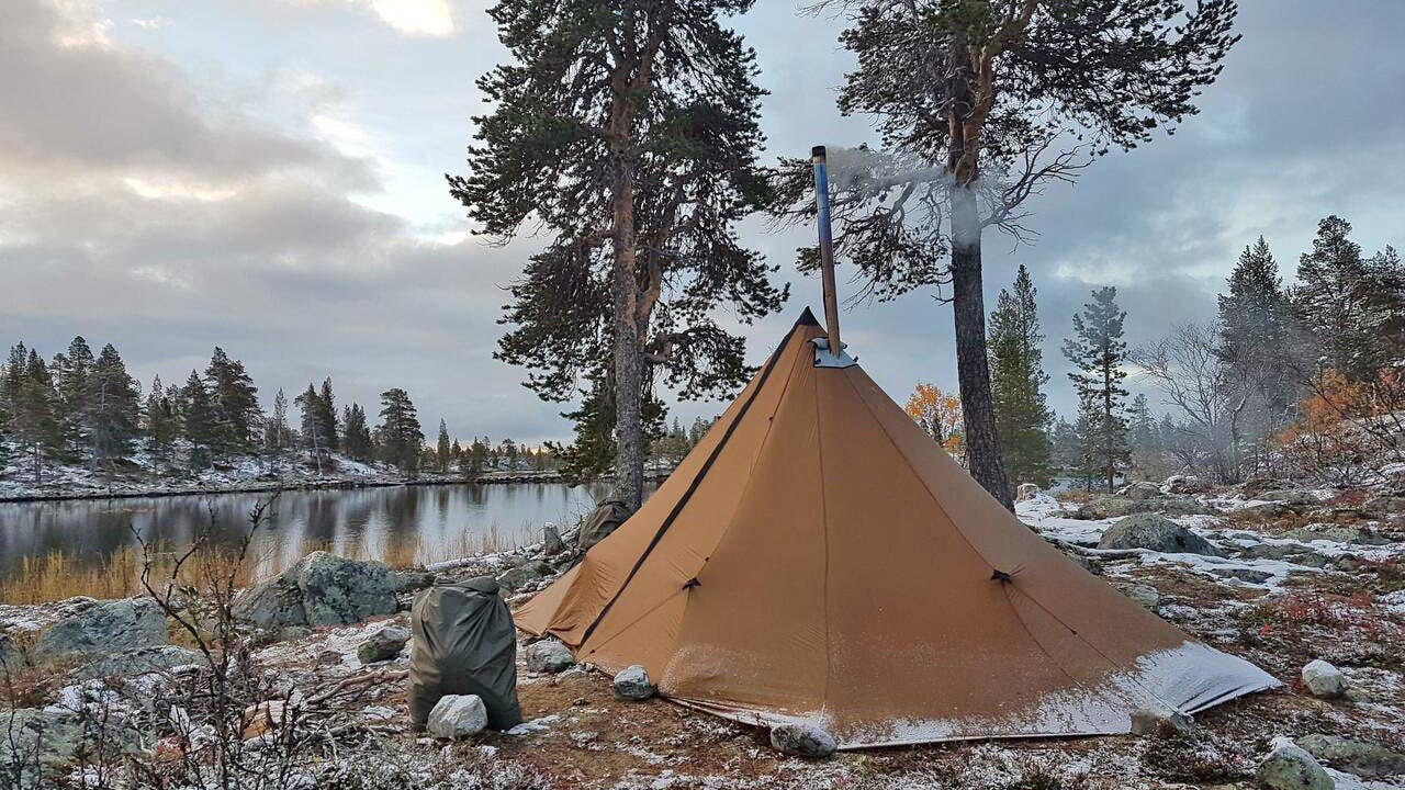 brown tent with chimney and smoke emerging from it near a snowy lake