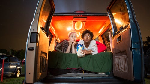 Couple holding popcorn while sitting in camping van during drive-in movie