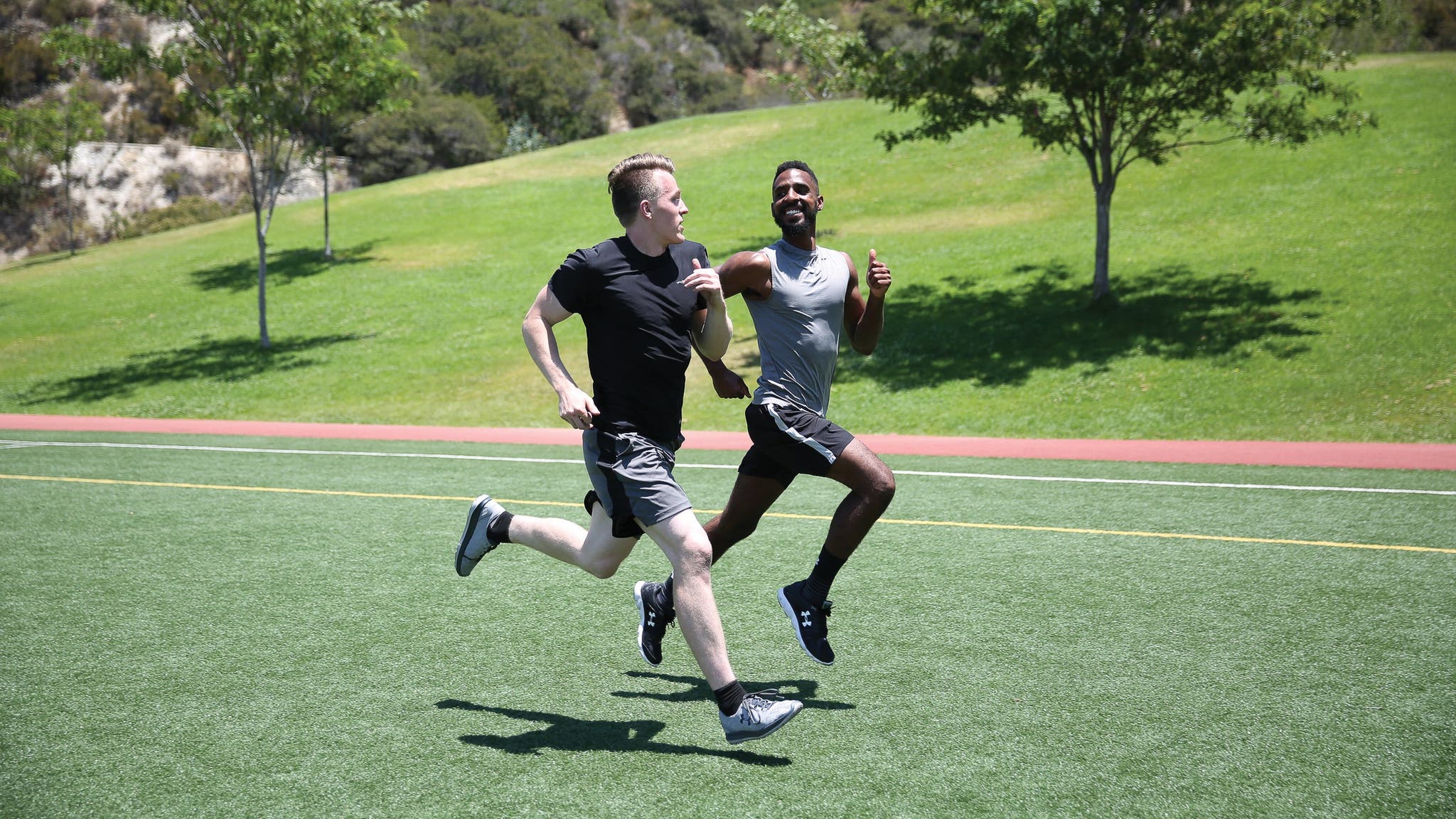 Two men running next to each other on grassy turf