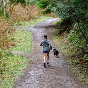 Woman running in green forest with a dog.