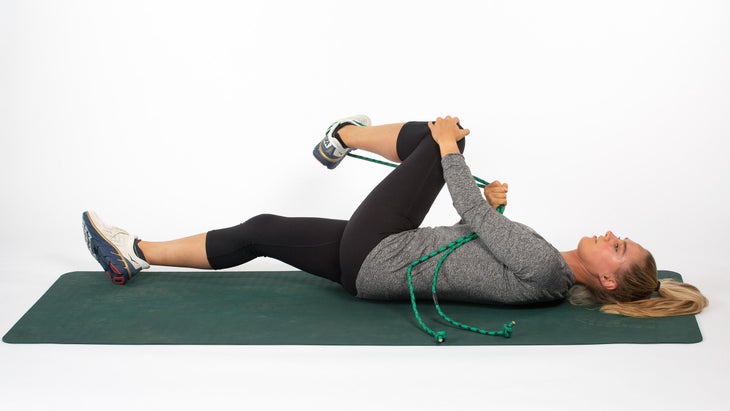 Woman lying on back using rope to stretch gluteals