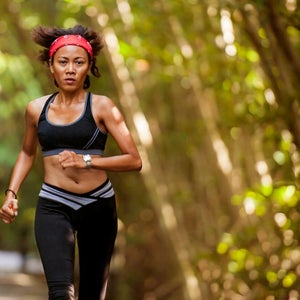 Outdoors portrait of woman with hairband training hard on asphalt road running workout at beautiful trees city park in exercise fitness and health care.
