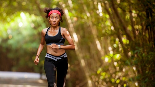 Outdoors portrait of woman with hairband training hard on asphalt road running workout at beautiful trees city park in exercise fitness and health care.