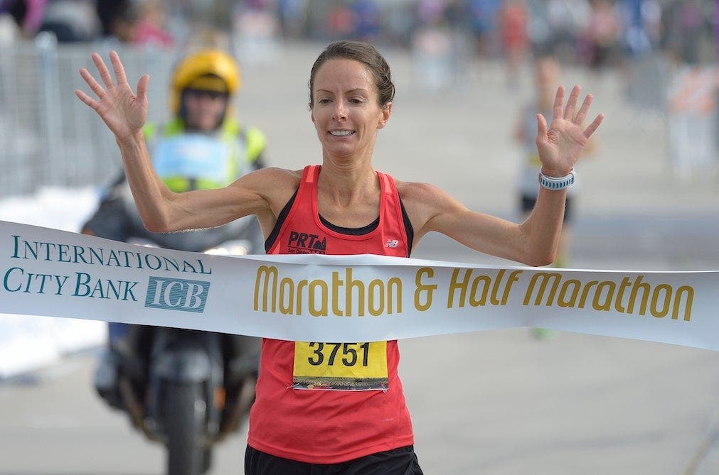 Hilary Corno crossing the finish line of a half marathon, breaking the tape.