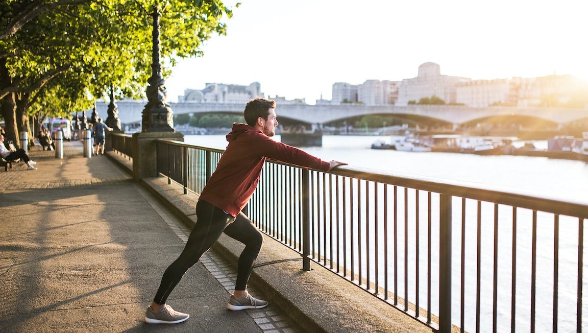 Male runner doing exercise by the river Thames in London, listening to music.