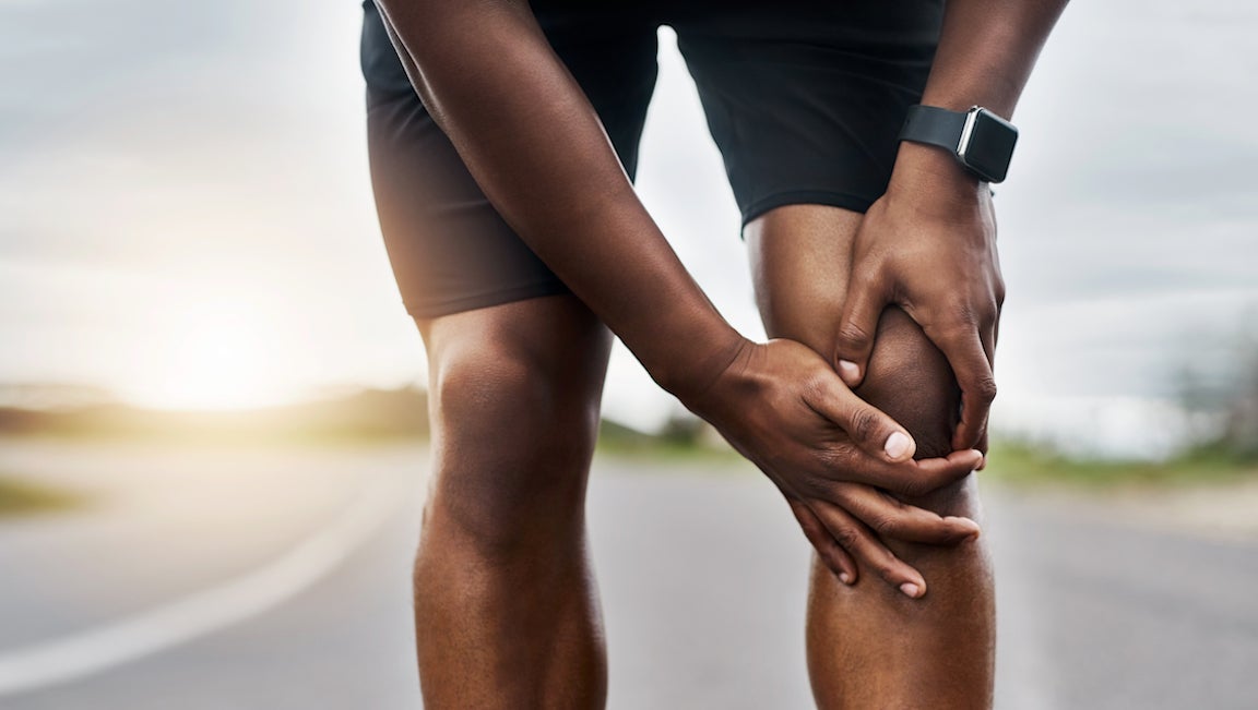 Closeup shot of a sporty man suffering with knee pain while exercising outdoors.