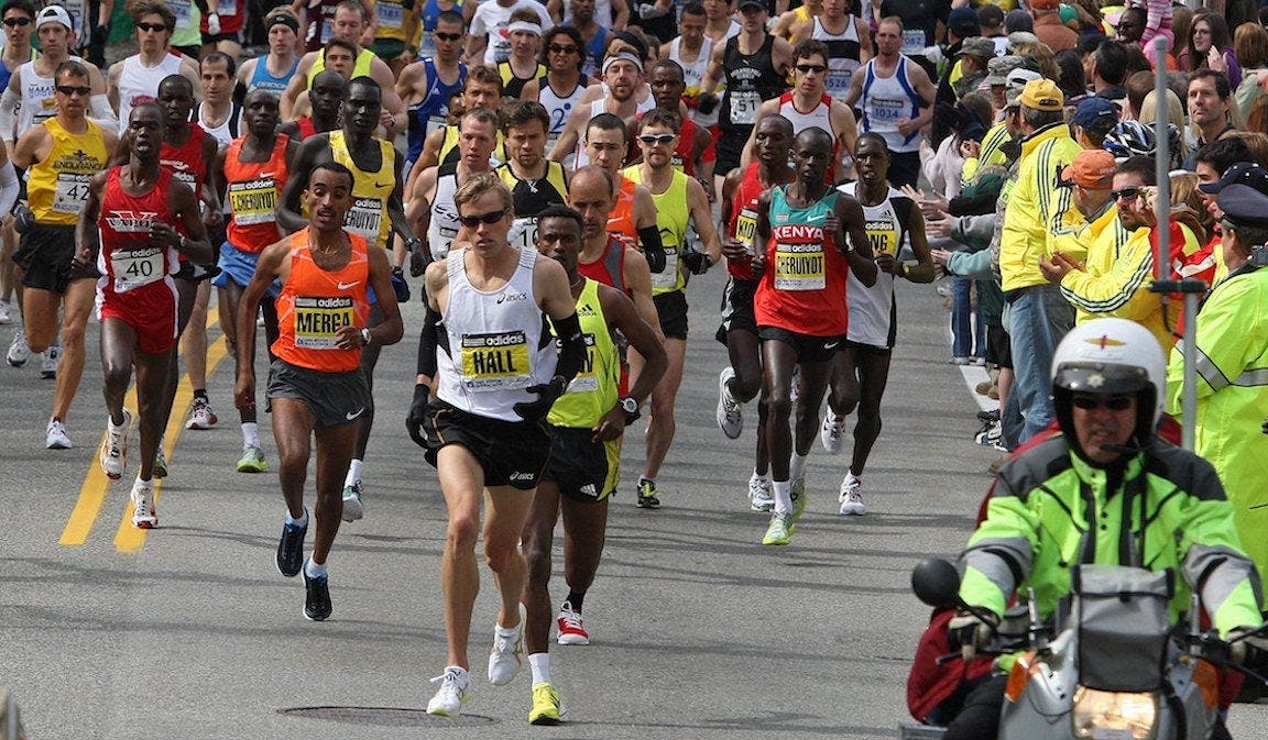 Ryan Hall leading the way in a white top at the Boston Marathon in a thick pack of runners right after the gun goes off.