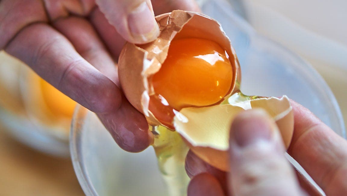 Person cracking open an egg with the yoke on full display.