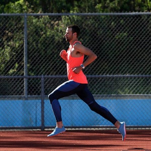 A male runner runs on a track on a sunny day.
