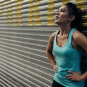Woman runner who is tired leaning against parking garage shutter in exhaustion.