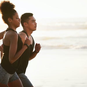 Shot of a young couple running along the beach