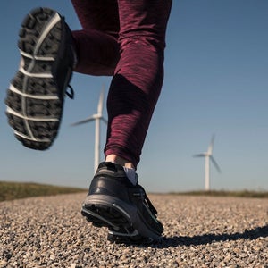 Young woman jogging on field way, wind wheels in the background.