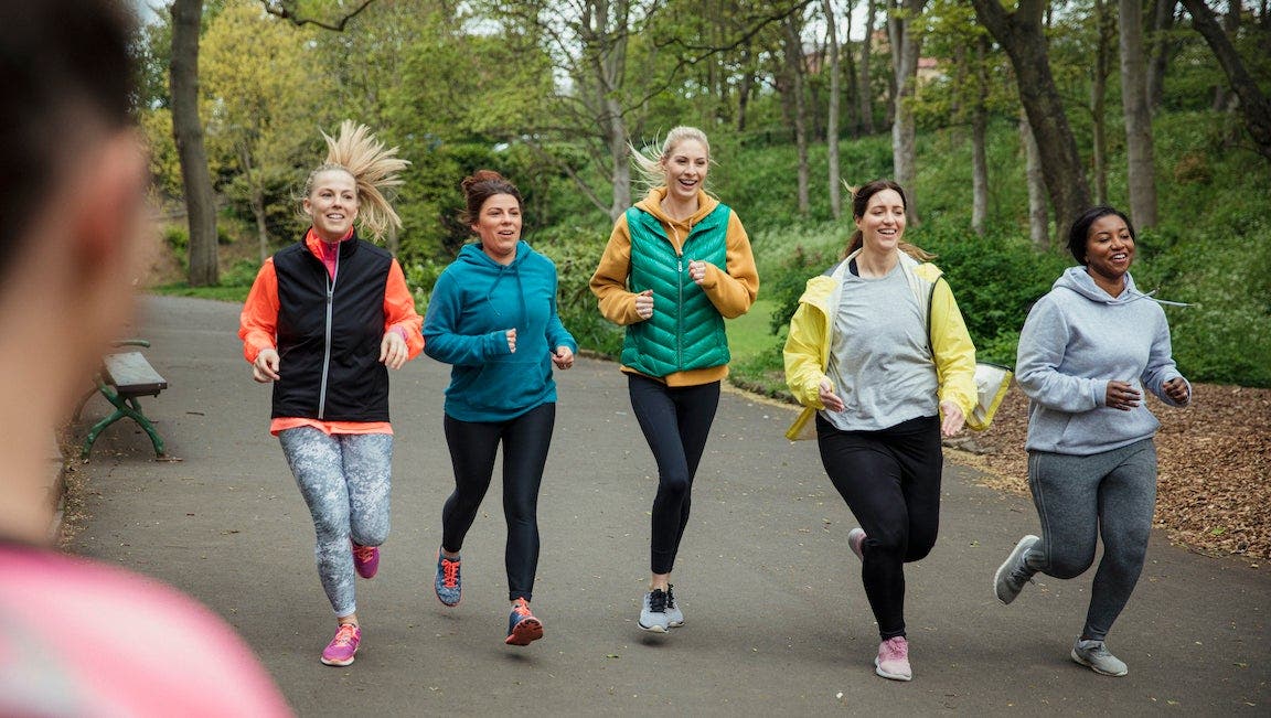 A group of women are running a workout as a coach (blurred) watches them.