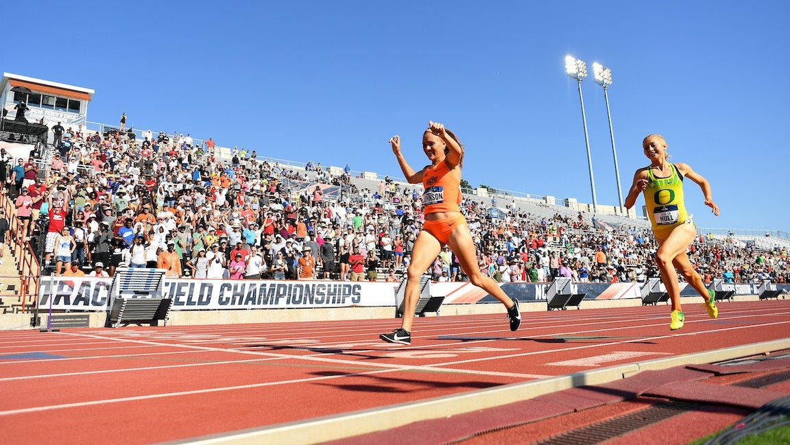 Sinclaire Johnson, in a bright orange uniform, raises her hands in victory as she crosses the finish line at the NCAA track and field championships in first place to win the 1500.