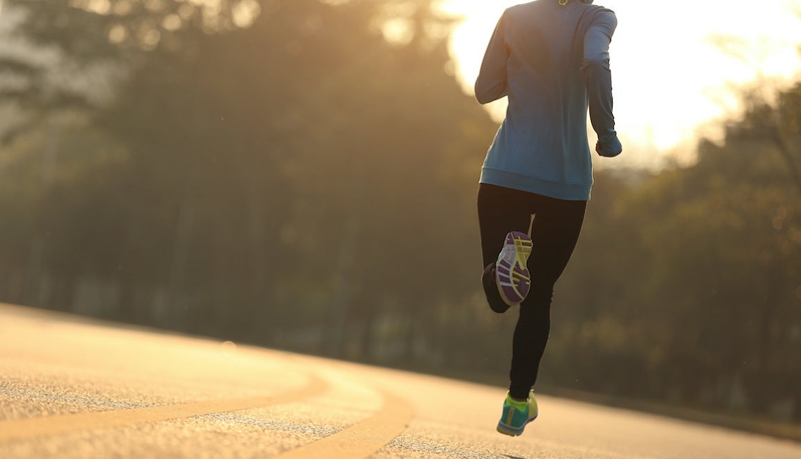 Young fitness woman runner running on sunrise road