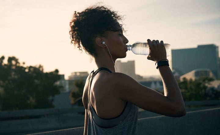Cropped shot of a woman wearing earphones and drinking water after her morning run in the city.