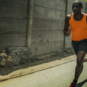 Fit professional sport man with athletic body running on city street pushing hard under harsh sun in urban background.