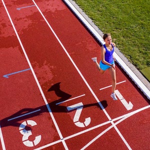 Aerial view of a female runner/athlete on a tartan track crossing finishing line.