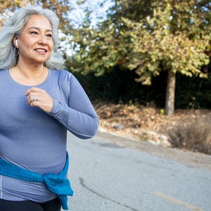 Woman jogging on a trail in purple long sleeved shirt.