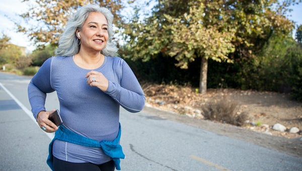 Woman jogging on a trail in purple long sleeved shirt.