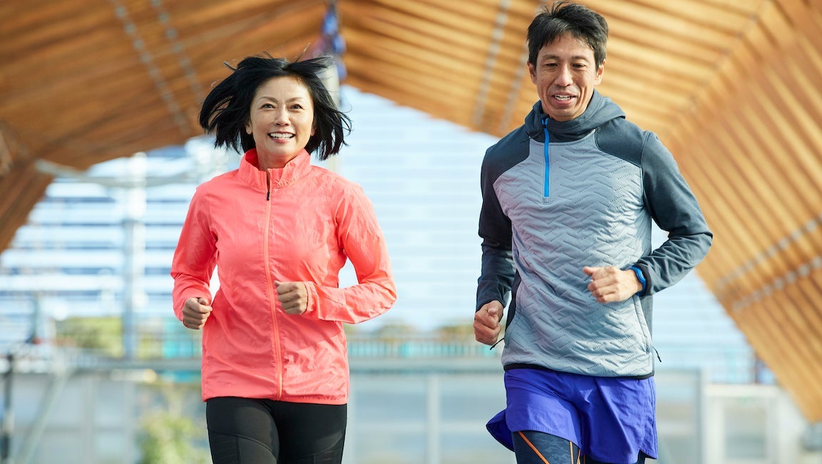 Japanese sportsman and sportswoman running together on track in a stadium.