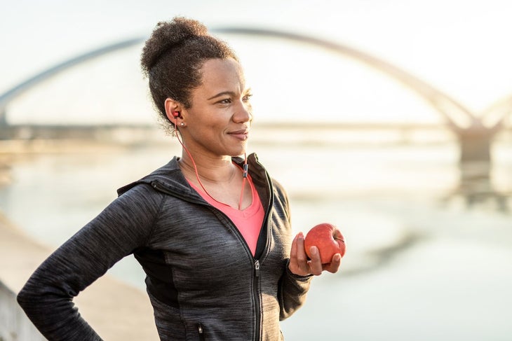 Happy athletic woman eating an apple after exercise.