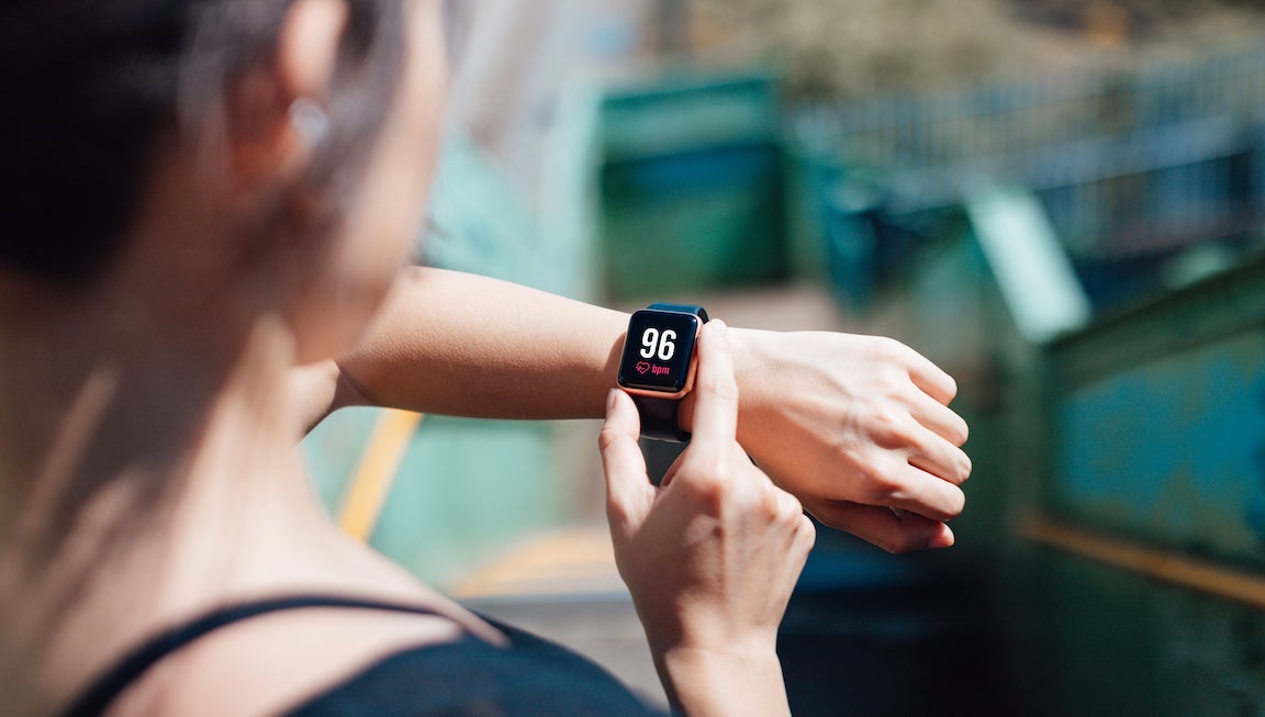 Over the shoulder view of a young woman wearing smart watch, using fitness app to check her training progress.