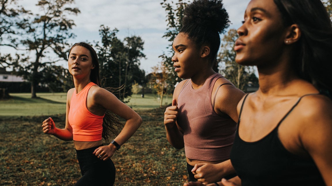 Group of woman train in a sunny park. Personal trainer shouts instructions and affirmations at her clients as they jog.
