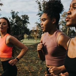 Group of woman train in a sunny park. Personal trainer shouts instructions and affirmations at her clients as they jog.