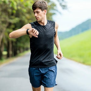White male athlete using wearable run tracking technology while jogging on the street.
