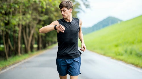 White male athlete using wearable run tracking technology while jogging on the street.