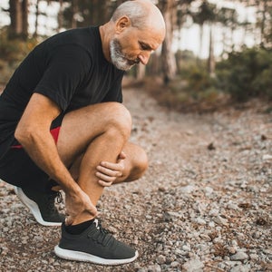Senior man holding ankle by hands looking like he's in pain.