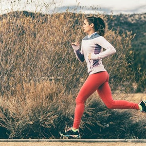 Side view of female athlete running by field.