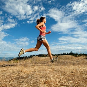 A woman trail running on a blue sky day with dramatic clouds.
