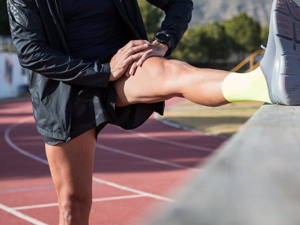 Anonymous male runner leaning on railing and stretching legs while warming up before training at stadium on sunny day.