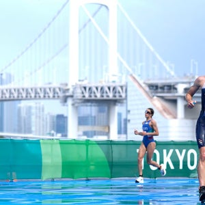 Woman triathlete races during the Tokyo 2020 Games with bridge in background.