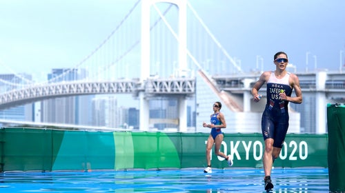 Woman triathlete races during the Tokyo 2020 Games with bridge in background.