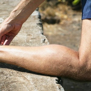 Man squeezing sore achilles while out running.