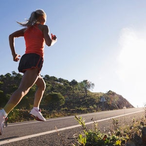 Blonde woman in pink top and old school Nike shoes running on an uphill road.