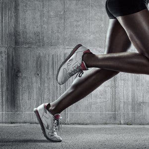 A low angle close up view of a female runners legs and feet running on concrete.