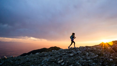 A woman trail running at as sunset along a mountain pass.