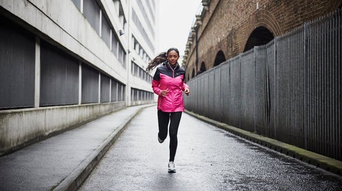 Female runner in pink rain jacket running in the city.