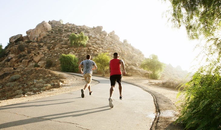 Two male friends running along mountain path up hill, rear view