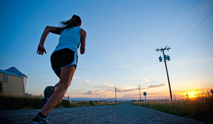 Woman running country road at sunrise/sunset past a telephone pole.