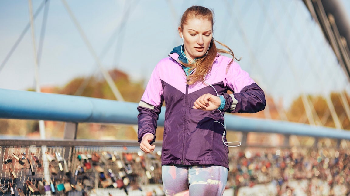 Adult female runner checking time whilst running across bridge in Paris.