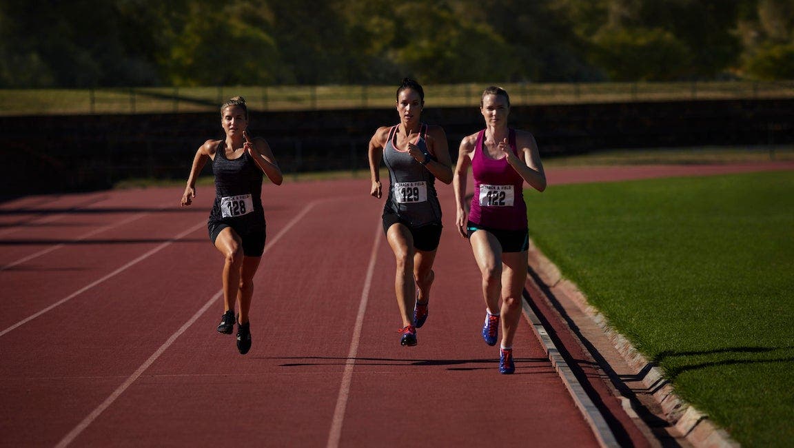 Runners racing at stadium during the day.