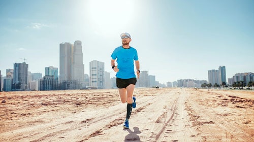Man running in hot desert. Sun beats down, skyscrapers in background. Looks like the United Arab Emirates.