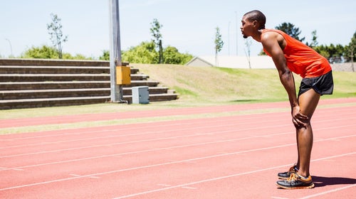 Tired athlete standing on running track on a sunny day.
